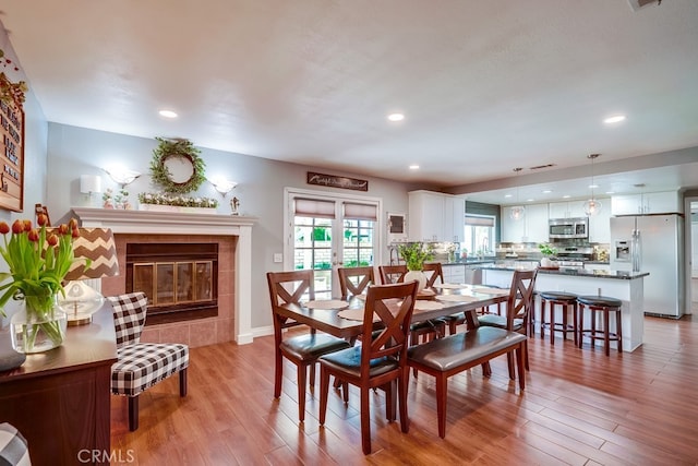 dining room with a tiled fireplace, baseboards, recessed lighting, and light wood-style floors