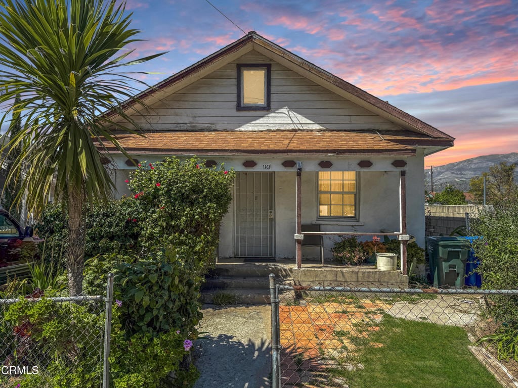 bungalow featuring a fenced front yard, a porch, stucco siding, a gate, and roof with shingles