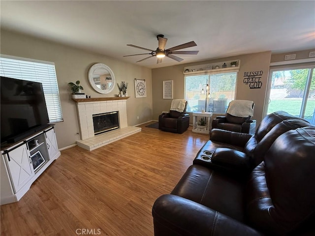 living room featuring light wood finished floors, ceiling fan, baseboards, and a fireplace