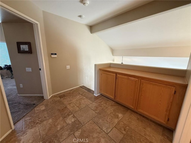 hallway featuring stone tile floors, baseboards, and vaulted ceiling with beams