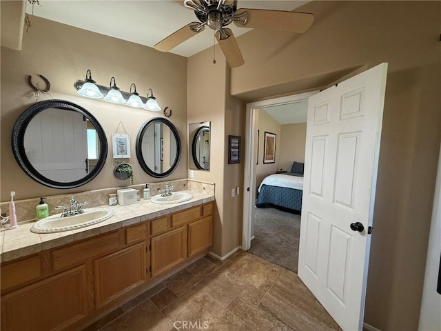 ensuite bathroom featuring baseboards, a ceiling fan, double vanity, and a sink