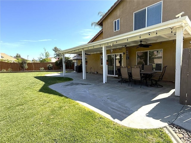 rear view of house with a patio, a yard, ceiling fan, stucco siding, and fence