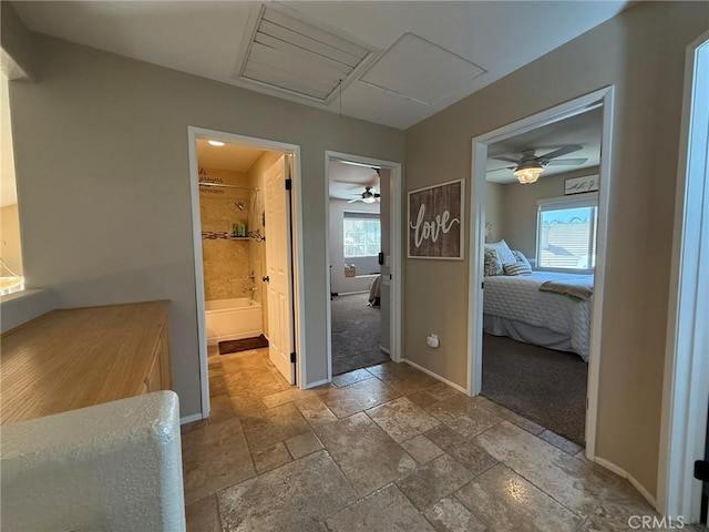 hallway featuring stone tile floors, baseboards, and attic access