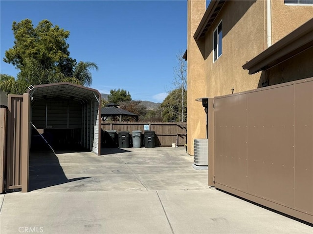 view of property exterior with central air condition unit, driveway, a detached carport, stucco siding, and fence