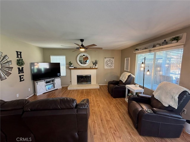 living area featuring baseboards, ceiling fan, a fireplace, and light wood-style flooring