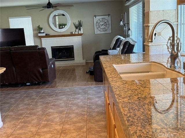 kitchen with a sink, a tiled fireplace, ceiling fan, wood finished floors, and open floor plan