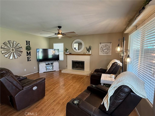 living area featuring plenty of natural light, wood finished floors, a tiled fireplace, and a ceiling fan