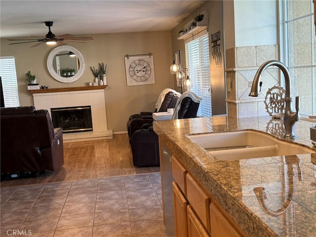 kitchen with a tile fireplace, open floor plan, ceiling fan, and a sink