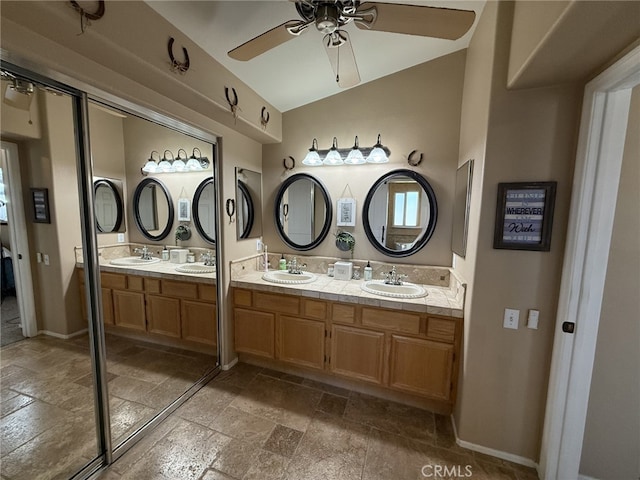 bathroom with vaulted ceiling, ceiling fan, stone tile flooring, and a sink
