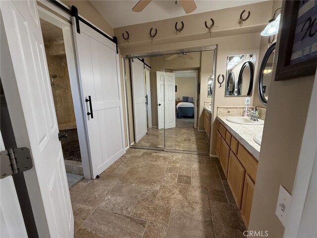 full bathroom with connected bathroom, stone tile flooring, ceiling fan, vanity, and a shower