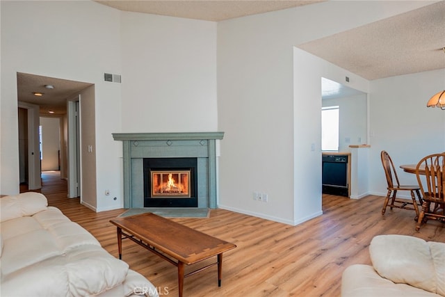 living room featuring light wood-type flooring, a glass covered fireplace, baseboards, and a textured ceiling