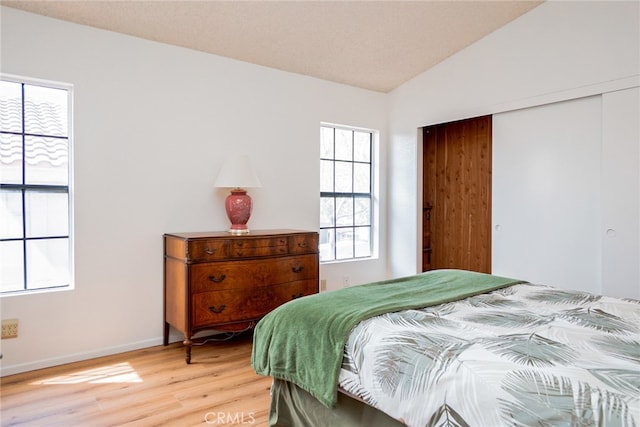 bedroom featuring light wood-style floors, a closet, multiple windows, and vaulted ceiling
