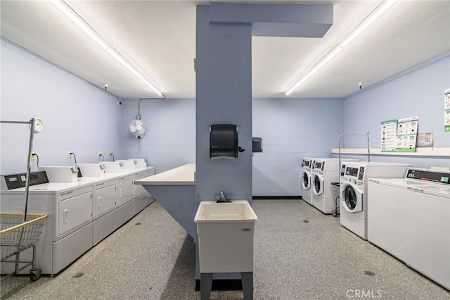 community laundry room featuring washing machine and clothes dryer and concrete block wall