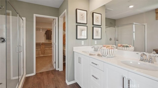 bathroom featuring a walk in closet, a sink, a stall shower, and wood finished floors