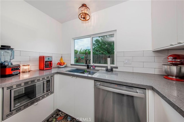 kitchen with white cabinets, appliances with stainless steel finishes, a sink, stone countertops, and decorative backsplash