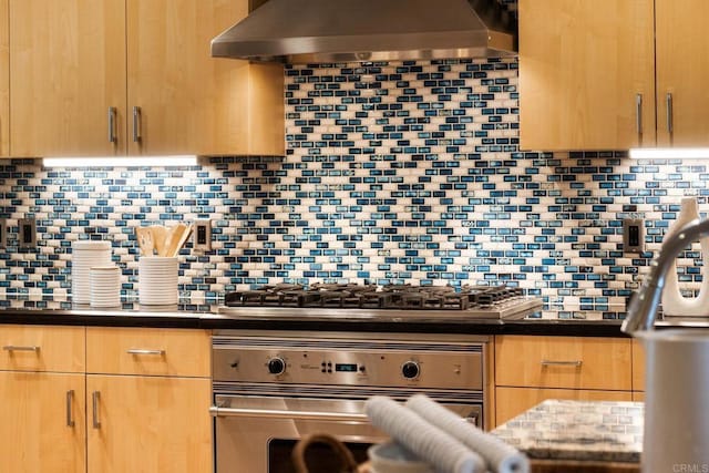 kitchen featuring wall chimney range hood, tasteful backsplash, dark countertops, stainless steel appliances, and light brown cabinetry