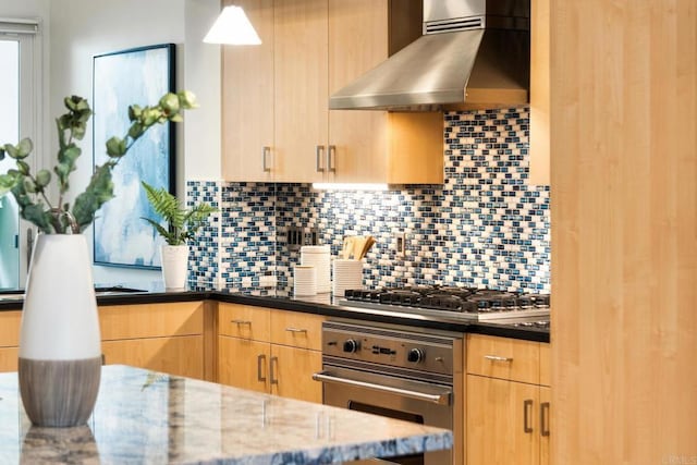 kitchen with dark stone countertops, stainless steel appliances, light brown cabinetry, wall chimney exhaust hood, and backsplash
