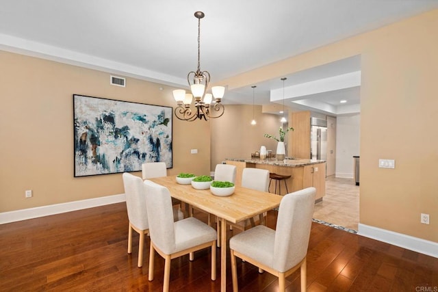 dining space featuring hardwood / wood-style flooring, a raised ceiling, visible vents, a chandelier, and baseboards