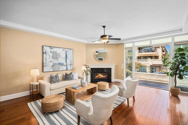 living area with dark wood-style floors, baseboards, ceiling fan, and a glass covered fireplace