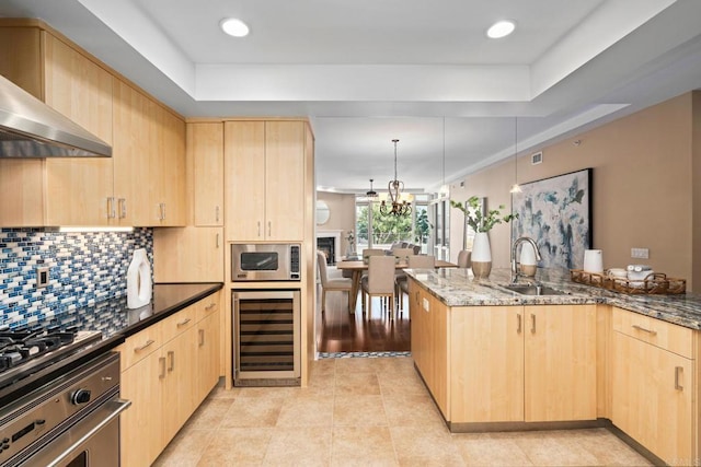 kitchen with beverage cooler, light brown cabinets, appliances with stainless steel finishes, a sink, and wall chimney exhaust hood