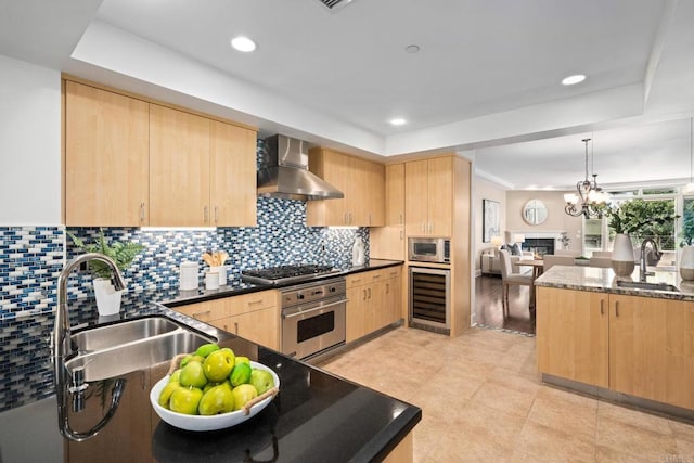 kitchen featuring light brown cabinets, stainless steel appliances, a tray ceiling, and wall chimney exhaust hood
