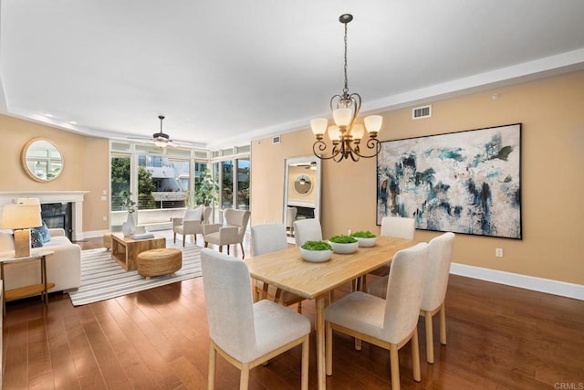 dining room featuring a premium fireplace, dark wood-style flooring, visible vents, baseboards, and ceiling fan with notable chandelier