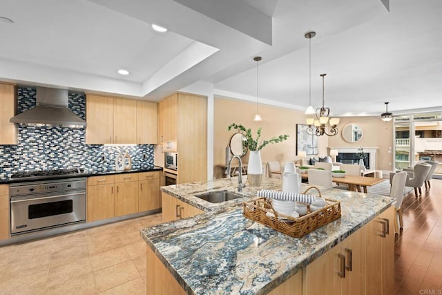 kitchen featuring decorative backsplash, a sink, light brown cabinets, stainless steel appliances, and wall chimney exhaust hood
