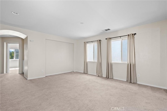 carpeted spare room with arched walkways, visible vents, and baseboards