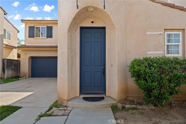doorway to property with stucco siding, driveway, an attached garage, a tile roof, and fence