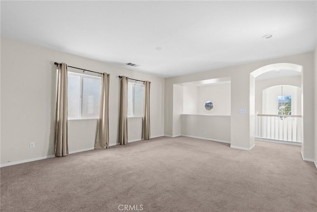 carpeted empty room featuring arched walkways, visible vents, and baseboards