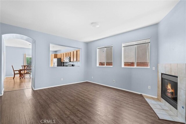unfurnished living room featuring baseboards, arched walkways, wood finished floors, and a fireplace