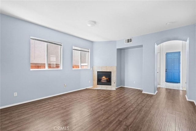 unfurnished living room featuring visible vents, baseboards, arched walkways, wood finished floors, and a tile fireplace