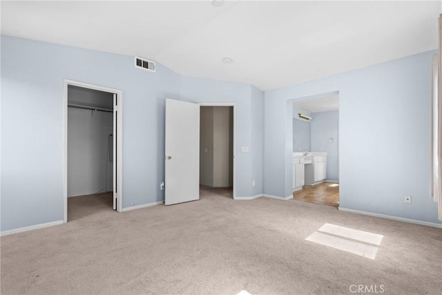 unfurnished bedroom with light colored carpet, a spacious closet, visible vents, lofted ceiling, and baseboards