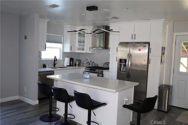 kitchen with visible vents, white cabinets, a sink, wall chimney range hood, and appliances with stainless steel finishes