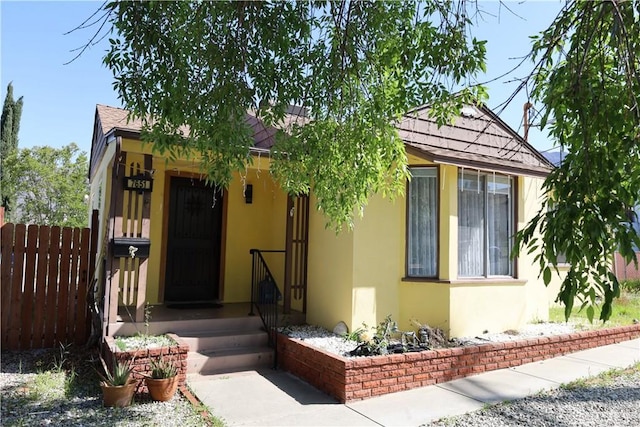 view of front of house featuring a shingled roof, stucco siding, and fence