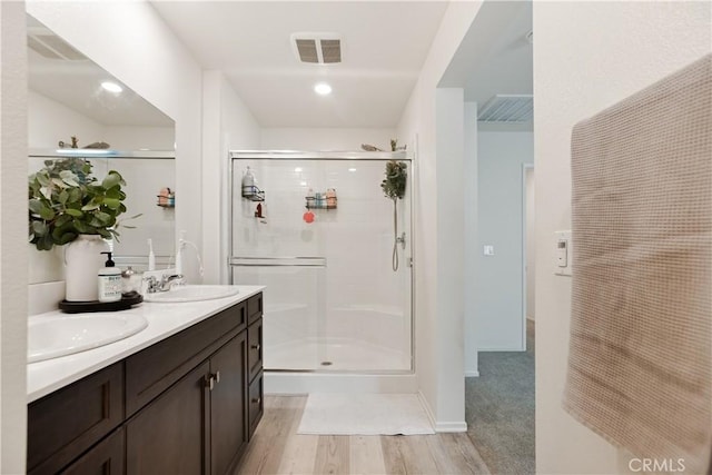 bathroom featuring a stall shower, visible vents, a sink, double vanity, and wood finished floors