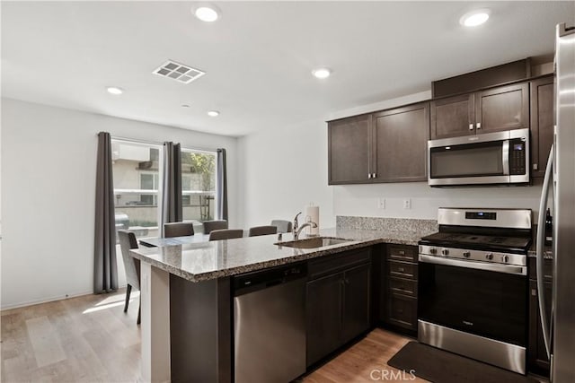 kitchen featuring dark brown cabinets, visible vents, a sink, a peninsula, and stainless steel appliances