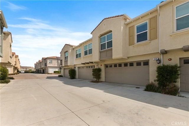 view of front of house featuring an attached garage, stucco siding, driveway, and a residential view