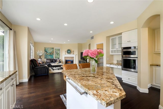 608 Chaparral Ct, Altadena, CA 91001 - kitchen featuring light stone countertops, stainless steel double oven, a glass covered fireplace, a center island, and dark wood-type flooring