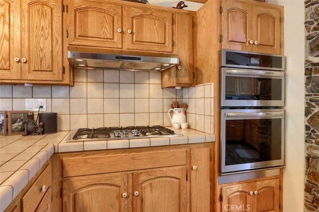 40957 Shandee Ln, Ahwahnee, CA 93601 - kitchen with backsplash, under cabinet range hood, brown cabinets, appliances with stainless steel finishes, and tile countertops
