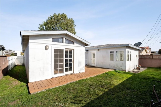 rear view of house featuring stucco siding, an outdoor structure, a fenced backyard, a deck, and a lawn
