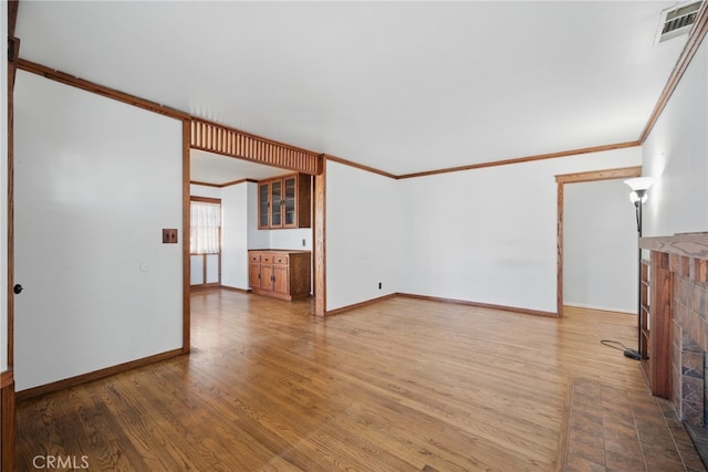 unfurnished living room with visible vents, baseboards, crown molding, and wood finished floors