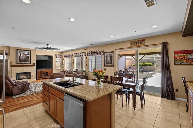 kitchen featuring a sink, dishwasher, ceiling fan, a fireplace, and visible vents