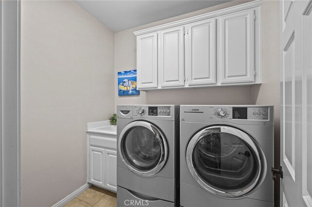 washroom featuring cabinet space, washing machine and clothes dryer, baseboards, and light tile patterned floors