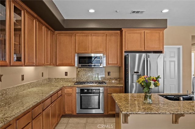 kitchen featuring light stone counters, visible vents, a sink, glass insert cabinets, and appliances with stainless steel finishes