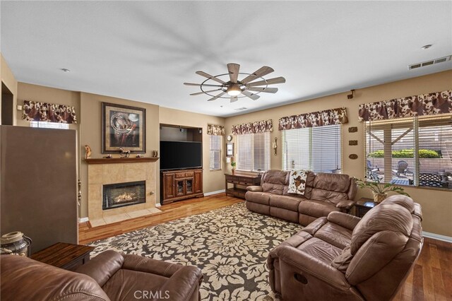 living room with wood finished floors, visible vents, a ceiling fan, baseboards, and a tiled fireplace