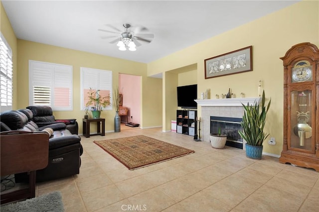 tiled living room with ceiling fan, a fireplace, and baseboards