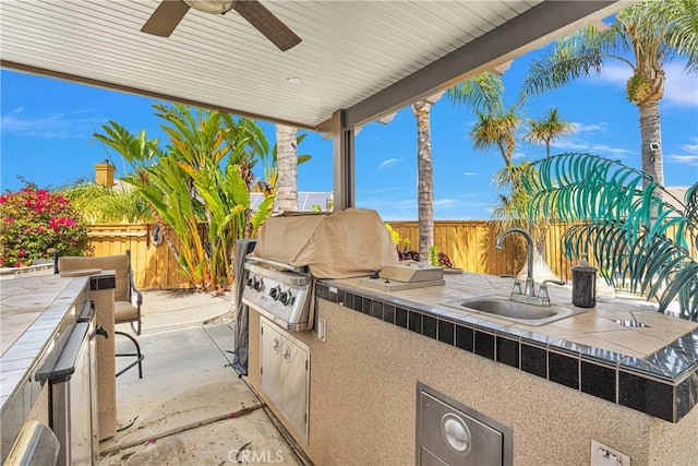 view of patio / terrace with grilling area, a fenced backyard, a sink, and a ceiling fan