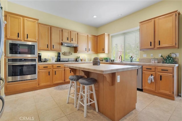 kitchen featuring a center island, a kitchen bar, under cabinet range hood, tile counters, and stainless steel appliances