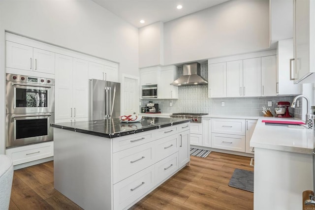 kitchen featuring decorative backsplash, appliances with stainless steel finishes, a sink, recessed lighting, and wall chimney exhaust hood